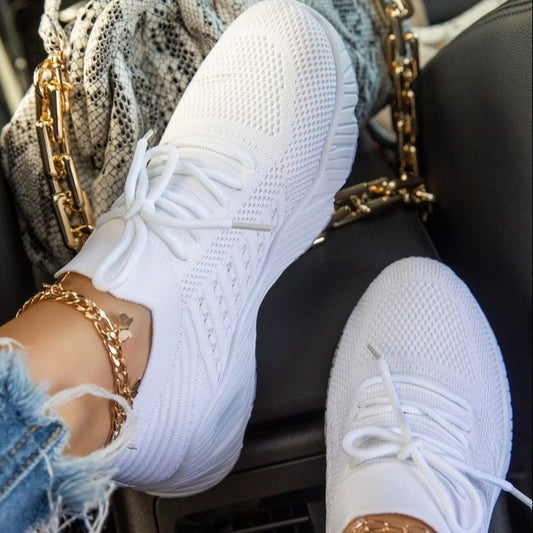 White sneakers worn with gold chains and denim jacket on a car seat.