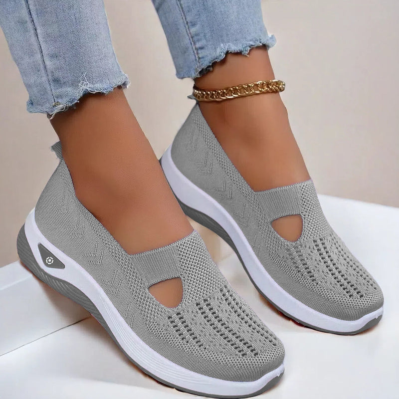 Women's Gray slip-on shoes with white soles worn with light blue jeans on a neutral background