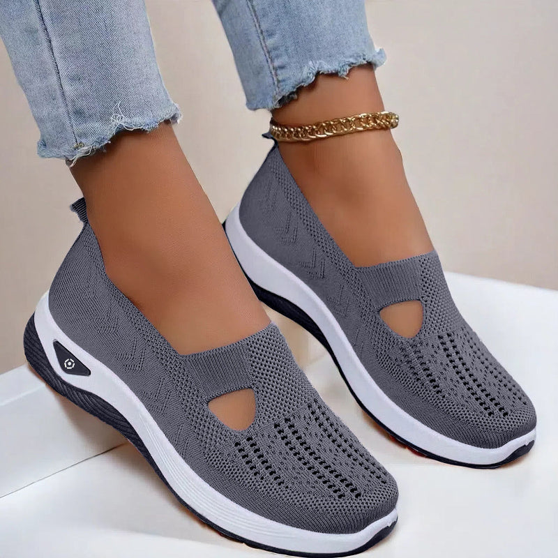 Women's Gray slip-on shoes with white soles worn with light blue jeans on a neutral background