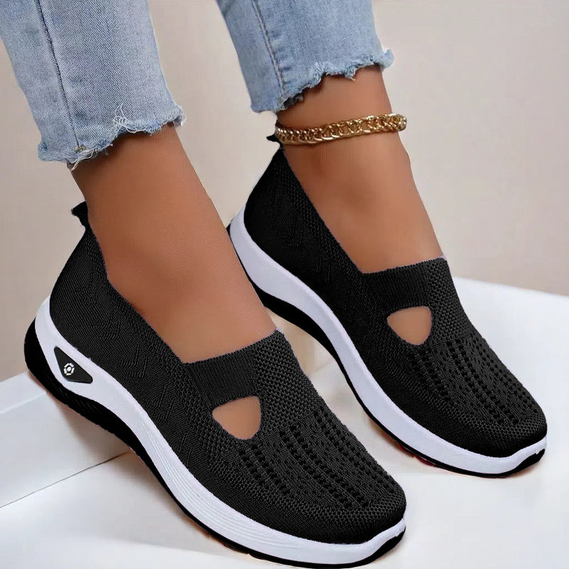 Women's Black slip-on shoes with white soles worn with light blue jeans on a neutral background