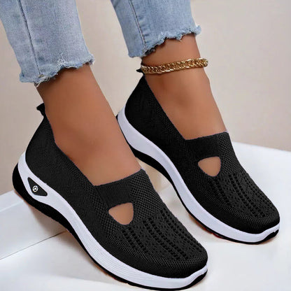 Women's Black slip-on shoes with white soles worn with light blue jeans on a neutral background