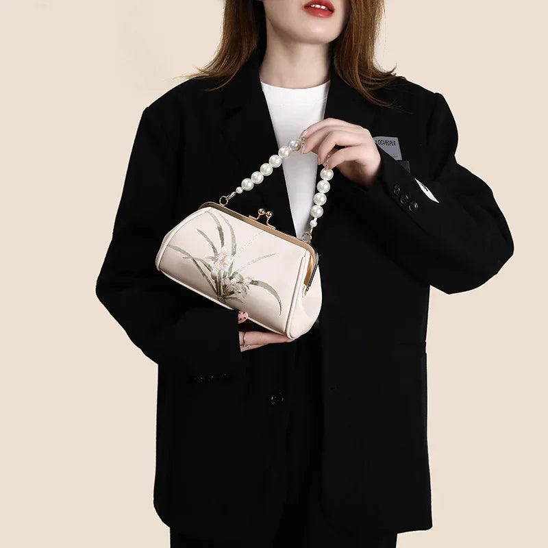 Beige framed shoulder bag with floral embroidery, pearl top handle, and chain strap