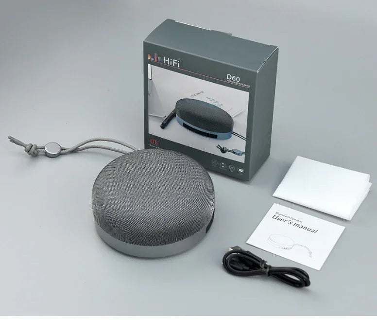 Grey cloth-covered Bluetooth speaker with hanging cord, shown with accessories