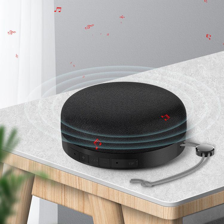 Black cloth Bluetooth speaker on a tabletop with visible control buttons