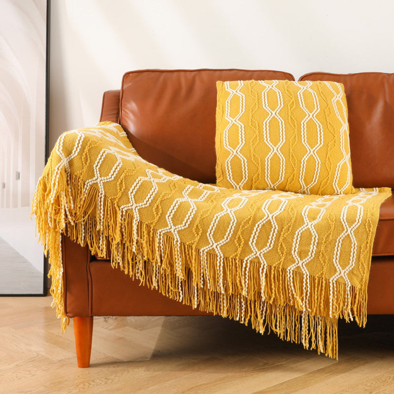 Yellow textured blanket with fringe draped over a brown leather sofa.
