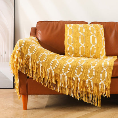 Yellow textured blanket with fringe draped over a brown leather sofa.