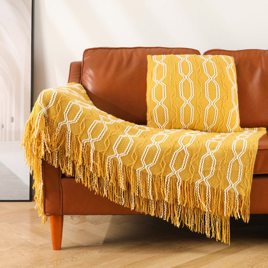 Yellow textured blanket with fringe draped over a brown leather sofa.