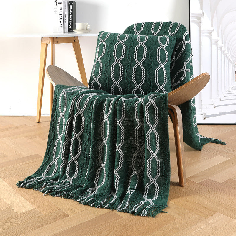 Green patterned throw blanket draped over a wooden chair on a wooden floor.
