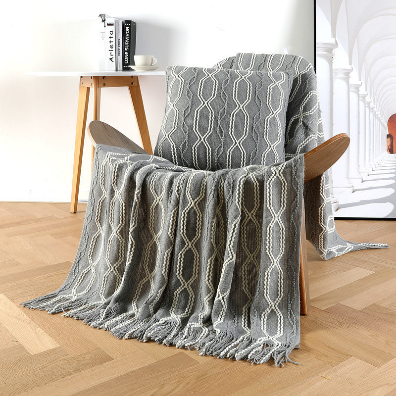 Gray patterned throw blanket draped over a wooden chair in a room with a table and books.