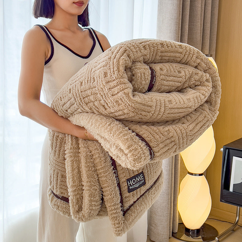 Beige plush velvet winter blanket with textured weave and dark-trim edge, rolled up