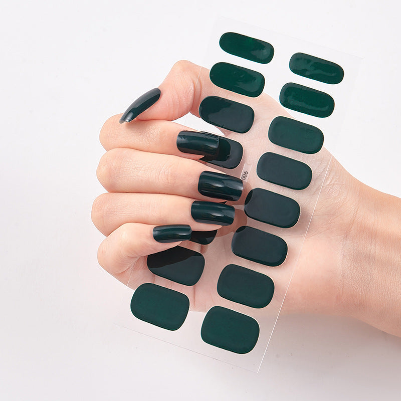 Hand with dark green nail polish holding a sheet of matching nail stickers on a light background