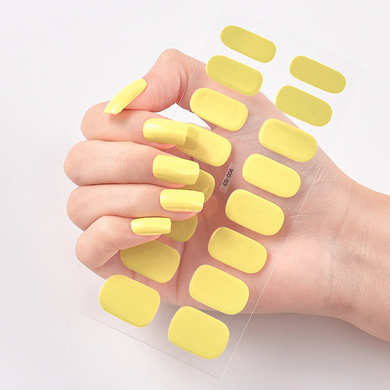 Hand wearing yellow nail polish with additional nail pads on a light background