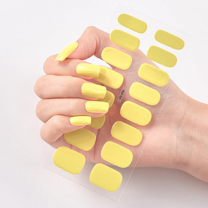 Hand wearing yellow nail polish with additional nail pads on a light background