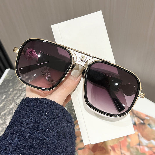 Sunglasses with gradient purple lenses held by a hand against a blurred background
