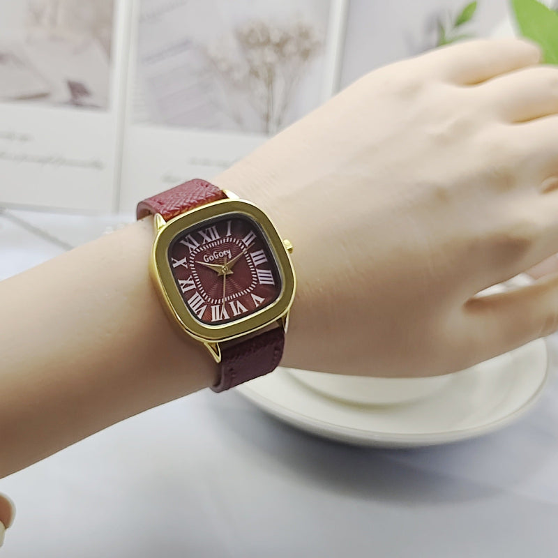 Women’s retro Roman dial leather strap watch on wrist, gold case with burgundy strap.