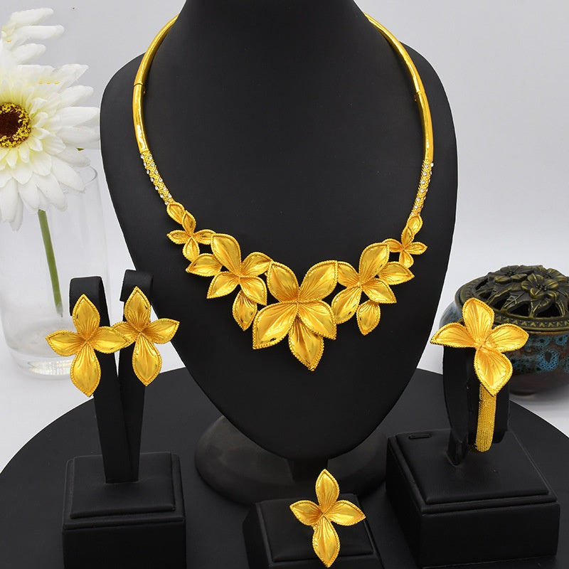 Gold floral necklace and earrings on a black stand with a white flower in the background
