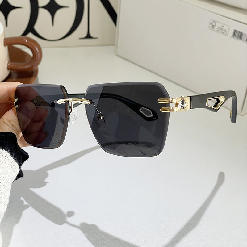 Sunglasses held near face, dark lenses, blue-gray frame, gold-tone geometric side detail