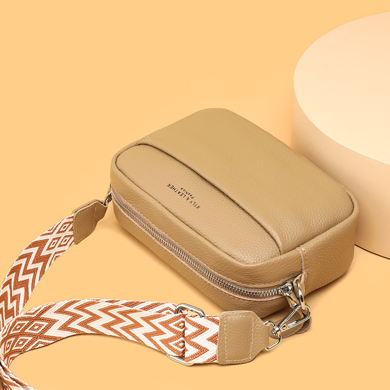 Beige compact crossbody bag with top handle loop, zip closure, and chevron strap