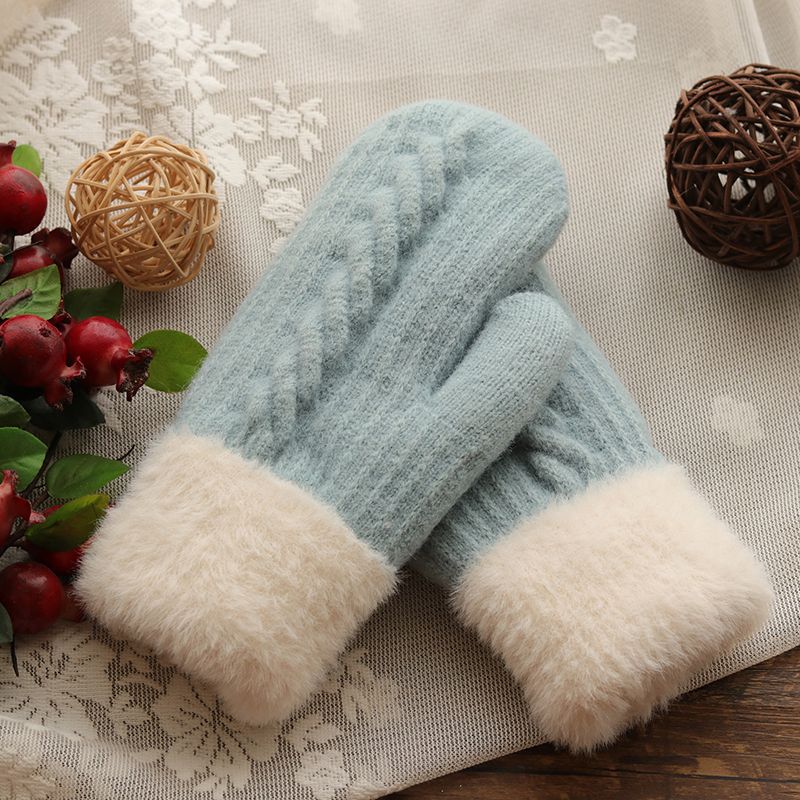 Light blue mittens with white cuffs on a decorative surface with flowers and a ball.