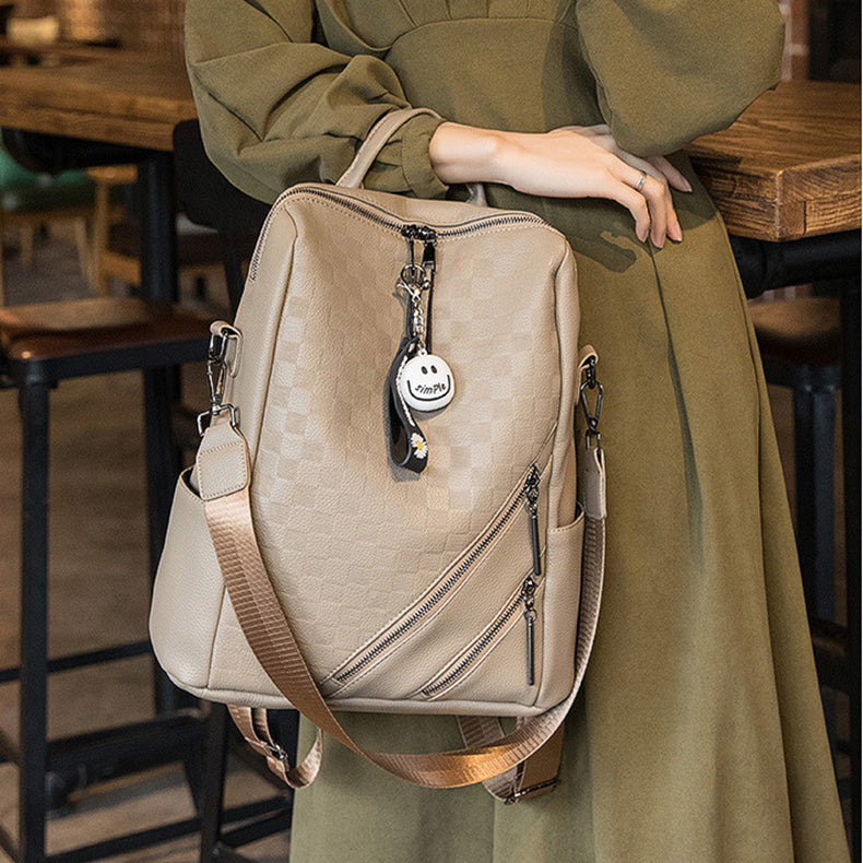 Person holding a beige backpack with a keychain in an indoor setting