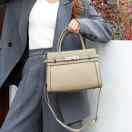 Person holding a beige handbag with a gray suit and blurred background