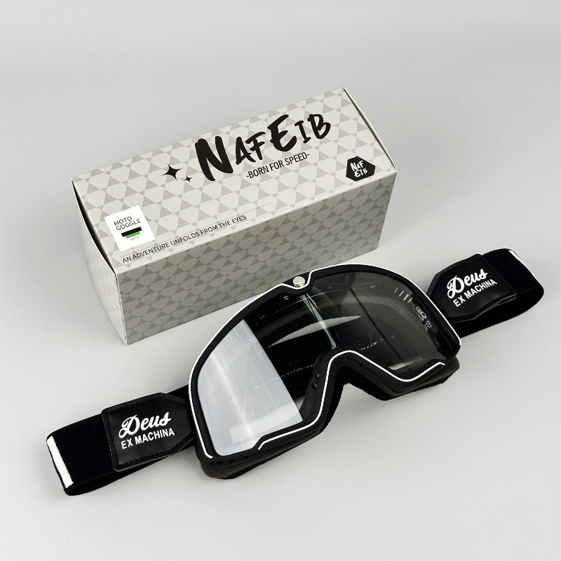 Black goggles with clear lens and black frame, placed in front of a branded box on a light gray background.