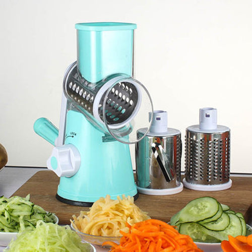 Turquoise rotary cheese grater with variously sliced vegetables on a wooden surface.
