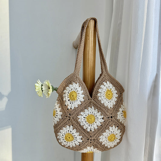 Crocheted bag with floral patterns on a wooden stand against a light curtain background