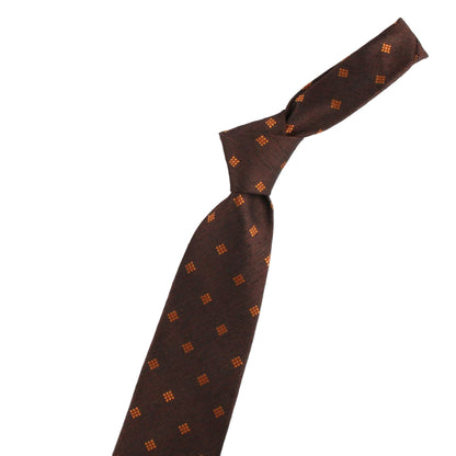 Brown tie with orange pattern, decorative clip, and small violin-shaped object on a white background