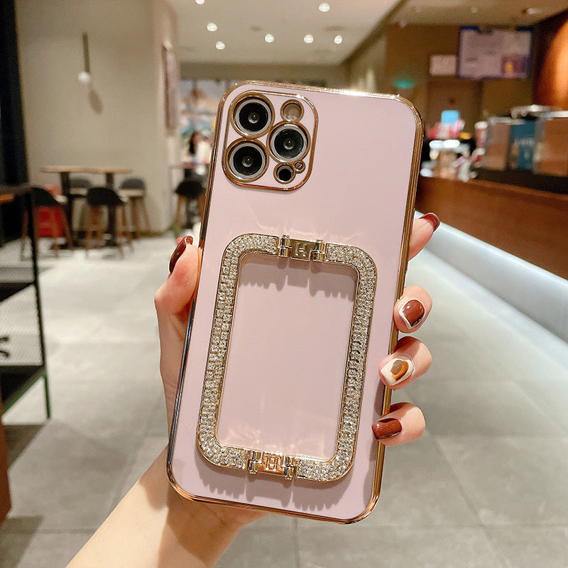 Pink phone case with rhinestone accents held by a hand in an indoor setting.