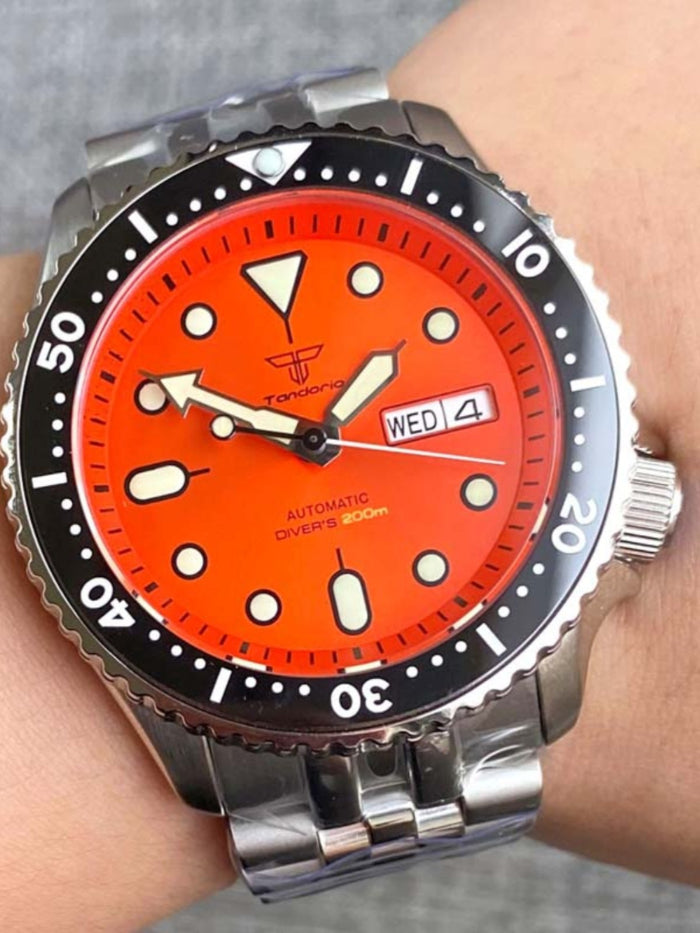 Wrist wearing a watch with an orange dial and silver case.