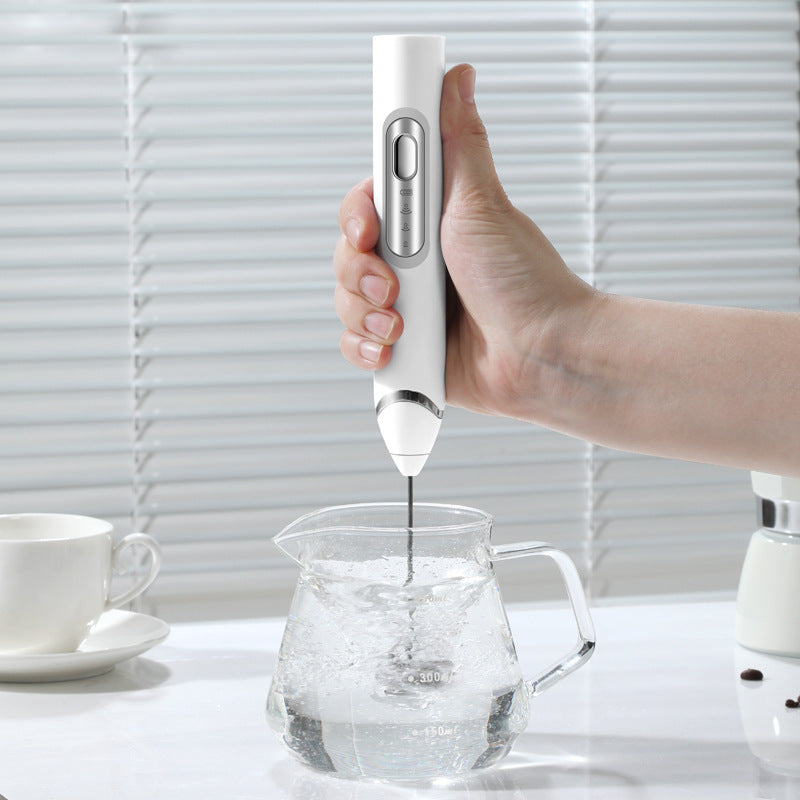 Handheld electric milk frother used to froth milk in a glass jug