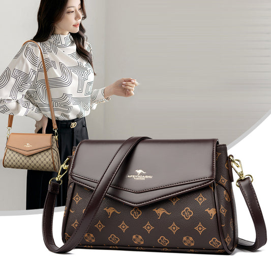 Brown patterned handbag with a visible brand logo, held by a person against a neutral background.