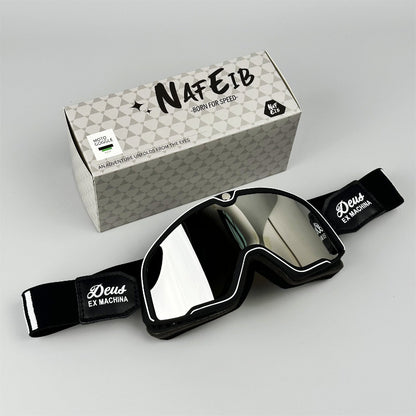 Black goggles with reflective lenses and 'Deus Ex Machina' branding, placed on a gray surface with a branded box in the background.