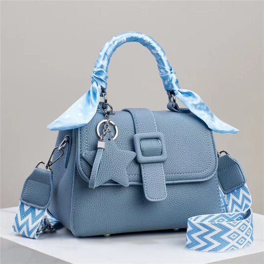 Blue handbag with matching strap and decorative bow on a neutral background