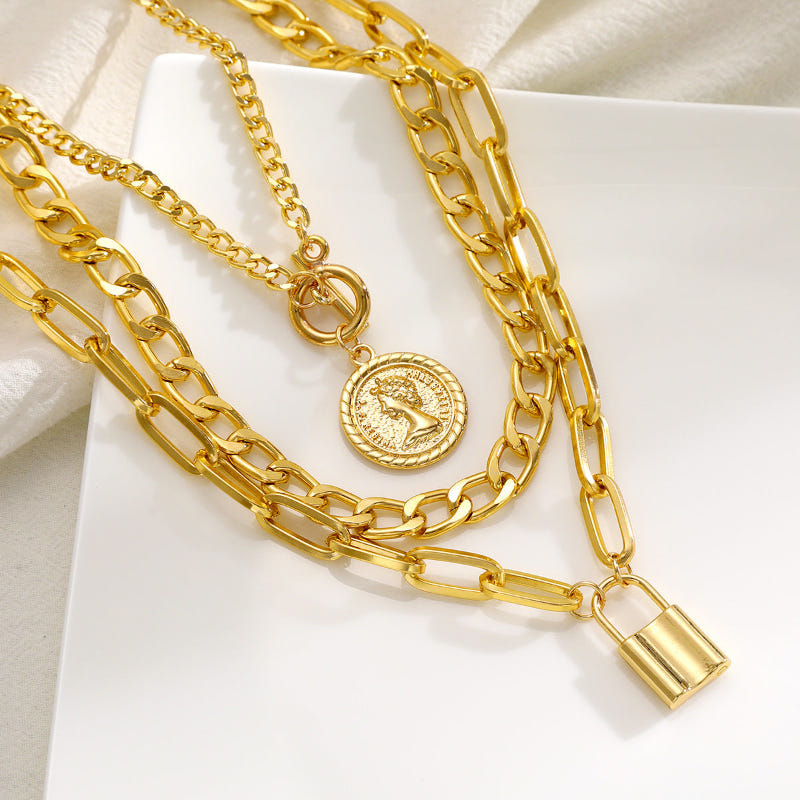 Close-up layered gold-tone chain necklace with circular medallion and padlock charm