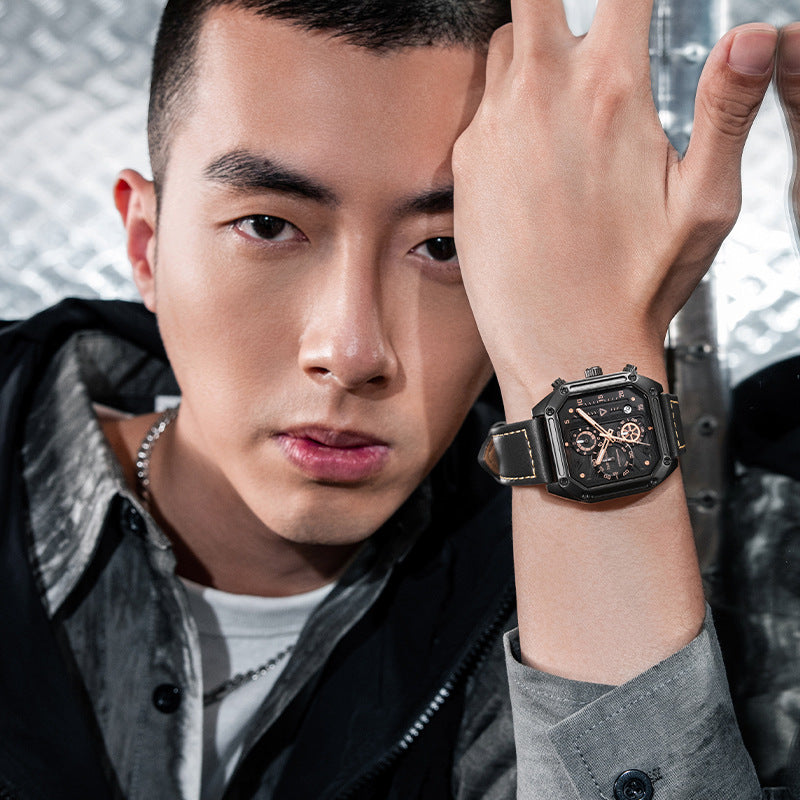 Man wearing a black wristwatch with a detailed face, posing against a neutral background.