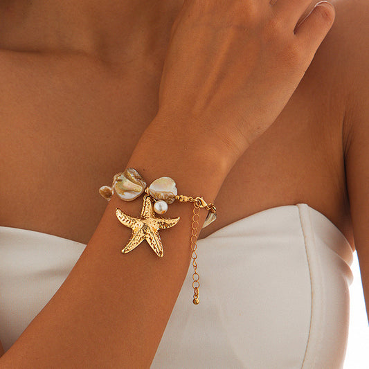 Women's Gold bracelet with starfish and shell charms on a wrist against a neutral background
