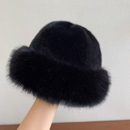 Black fur hat held by a hand against a plain background