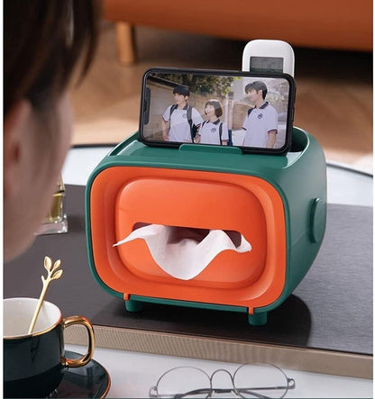 Retro TV tissue box in green and orange, with tissues dispensing and a phone resting on top.