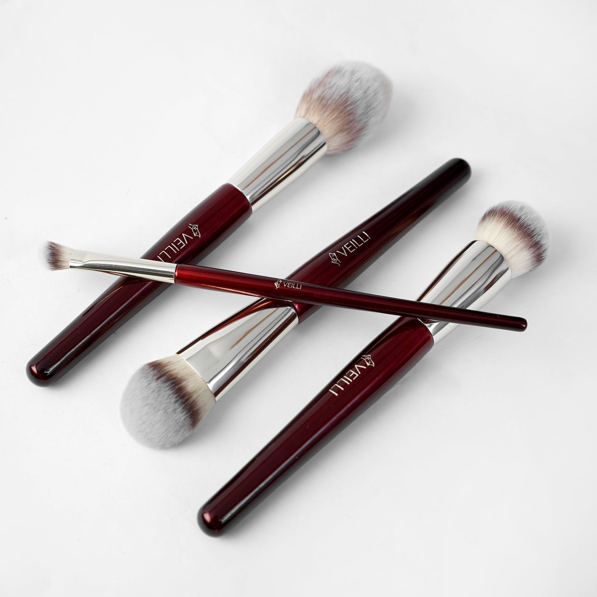 Four burgundy makeup brushes with silver ferrules and varied brush heads
