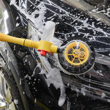 Rotating washing brush with yellow pole scrubbing a soapy car surface