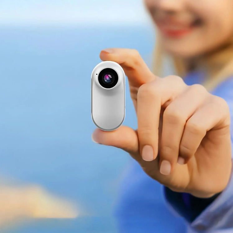 Mini-Motion View white motion camera held between fingers, showing its front lens