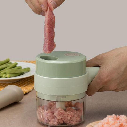 Green mini food chopper with transparent bowl and blade, being held while chopping