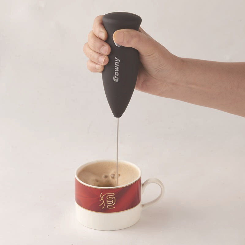 Black electric milk frother with a slim metal whisk held over a coffee cup