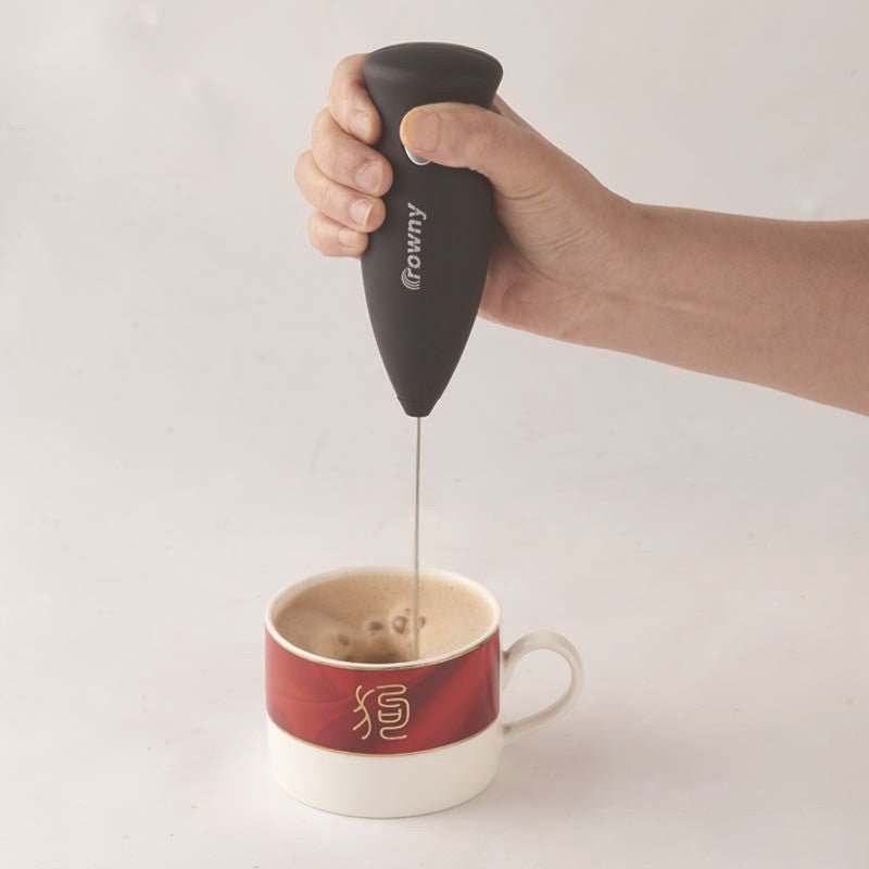 Black electric milk frother whisking a drink in a ceramic cup.