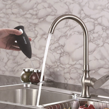 Black electric milk frother held under running water for rinsing.