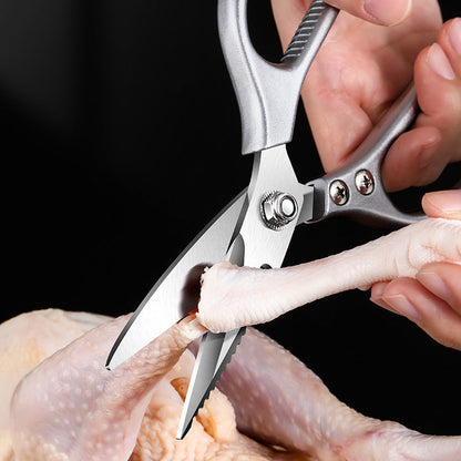 Silver kitchen scissors cutting a raw chicken joint.