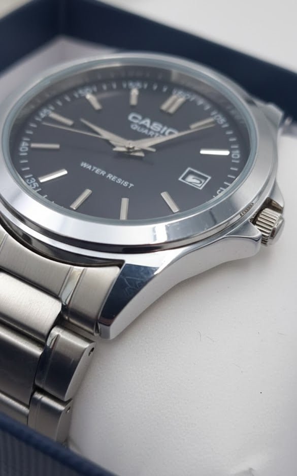 Casio watch close-up showing dark dial, date window, polished case, and metal bracelet