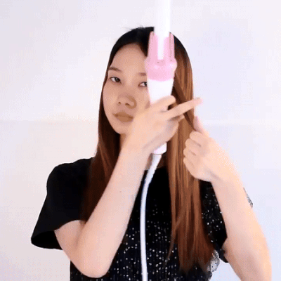Woman using a white and pink hair curler on a section of hair